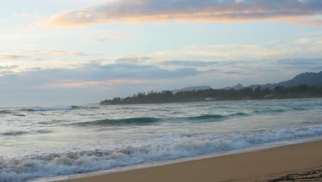 Hand-held-view-of-a-sunset-on-a-Hawaii-beach-on-North-Shore-Hawaii-with-pink-orange-clouds-and-tropical-forest-on-a-peninsula-in-the-background