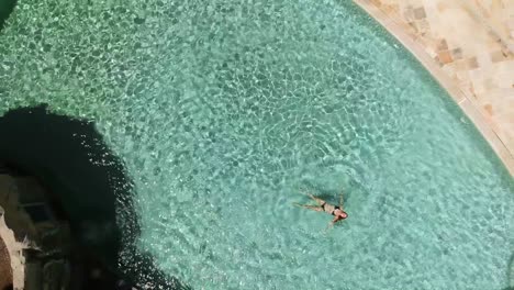 Top-down-birds-eye-view-drone-shot-of-a-girl-in-a-bikini-floating-in-a-large-pool-at-a-resort-in-Australia
