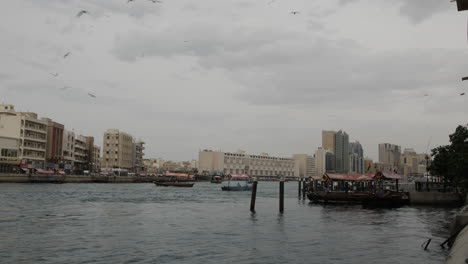 Der-Fluss-Im-Alten-Dubai-In-Den-Vae-Mit-Mittleren-Osterbooten-Und-Möwen,-Die-An-Einem-Bewölkten-Und-Bewölkten-Tag-über-Uns-Fliegen
