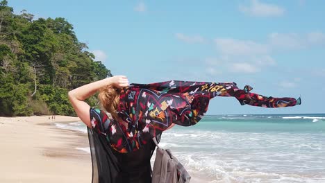 A-blond-woman-filmed-in-slow-motion-lifts-a-scarf-over-her-head-in-the-wind-on-a-remote-beach-in-the-Andaman-islands