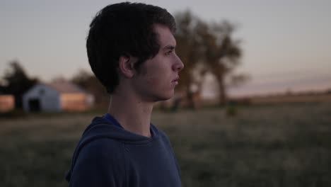 Side-medium-shot-of-a-young,-teenage-boy-watching-the-sun-set-in-a-Kansas-field