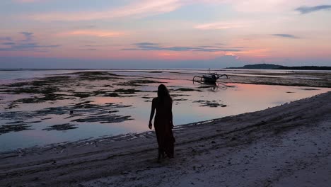Beautiful-slow-motion-silhouette-shot-of-a-young-women-walking-down-a-tropical-beach-during-sunset-on-the-Gili-islands,-in-Indonesia