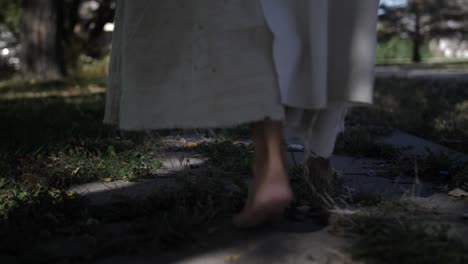 A-dramatic-slow-motion-closeup-of-Jesus'-feet-walking-down-a-sidewalk-while-he-wears-a-white,-tattered-robe