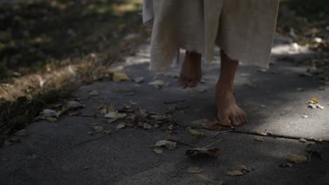 A-closeup-shot-of-a-man-dressed-as-Jesus-Christ-wearing-a-white,-tattered-robe-walks-in-dramatic-slow-motion-on-a-sidewalk