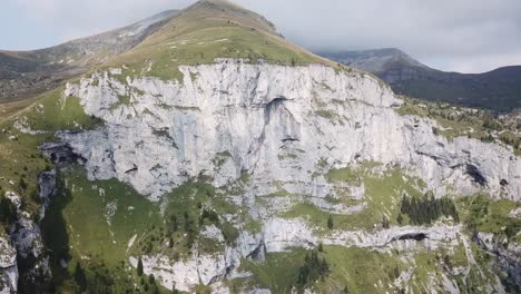 Big-white-cliff-of-in-italian-dolomites-with-overcast-weather-in-the-background-and-green-fields-on-top
