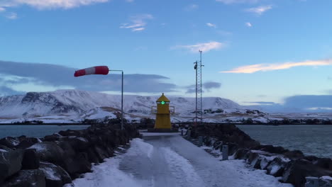 Yellow-Lighthouse-on-Jetty-at-Reykjavik-Ferry-Terminal,-Snowy,-Windy-Morning-with-Mountains-and-Sea