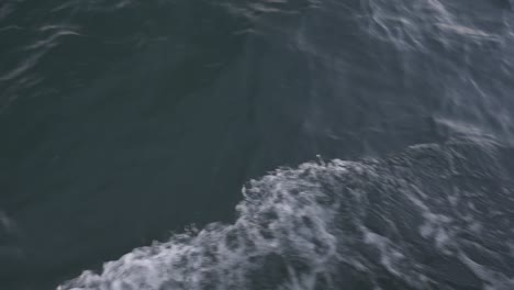 waves-from-a-boat-moving-in-the-ocean,-camera-onboard-handheld,-camera-tilt-up