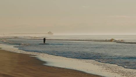 Wide-shot-showing-mystic-misty-atmosphere-at-beach-with-crashing-waves-and-jetty-in-background