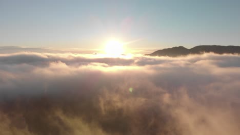 Aerial-descent-into-foggy-valley-sunrise,-sun-over-misty-sea-of-cloud