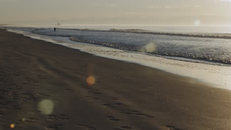 Lens-Flares-Bei-Schönem-Sonnenaufgang-Am-Strand-Mit-Ruhigen-Meereswellen,-Die-Den-Sandstrand-Erreichen