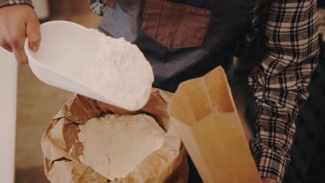 Baker-dumping-flour-from-a-sack-into-a-carton-bag-in-slow-motion