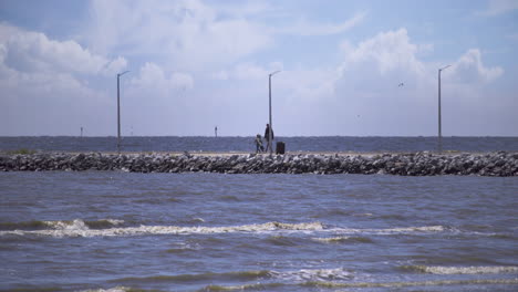 A-father-and-son-walk-along-a-stone-pier-in-with-fishing-gear-in-hand-on-a-beautiful,-sunny-day-in-Gulfport,-Mississippi