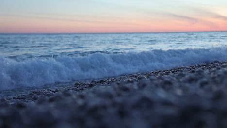 Sea-wave-washing-pebbles-beach-in-slow-motion-during-colorful-sunset