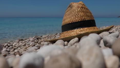 Closeup-of-straw-hat-on-pebbles-beach-with-blurry-background-of-Mediterranean-sea