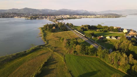 Aerial-drone-shot-tilting-up-and-showing-SBB-train-driving-towards-Rapperswil-Switzerland-on-a-summer-evening
