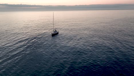 An-aerial-sunset-shot-of-sea-waters-revealing-a-boat-with-a-lowered-sail