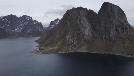 Aerial-view-of-massive-mountains,-rising-from-the-sea,-in-cloudy-Lofoten,-Norway---pan,-drone-shot