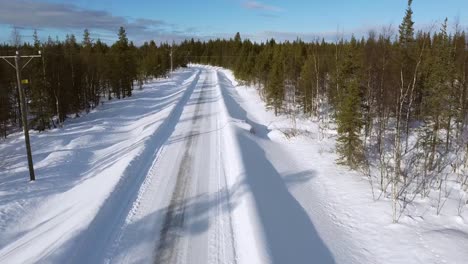 Snowy-road-through-conifer-forest-leading-to-Levi-mountain,-Lapland,-finland,-revealing-aerial-shot