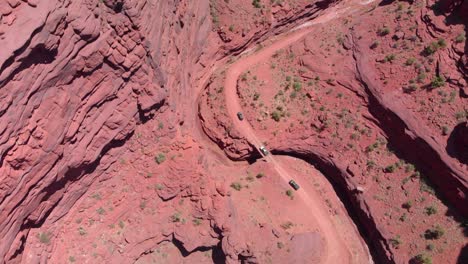 Red-sandstone-cliffs-form-deep-canyon:-Vehicles-on-road-in-Moab,-Utah