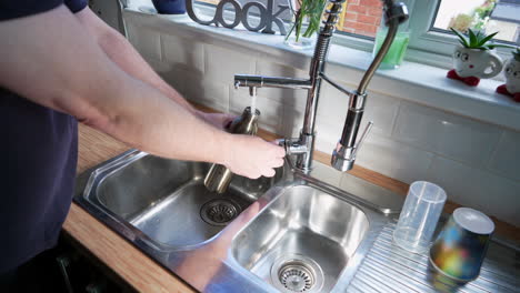 Filling-water-bottle-from-faucet-tap-and-screwing-lid-cap-back-on-male-hand