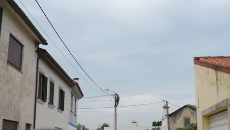 Static-view-of-man-working-on-an-electricity-pole,-on-suburban-cityscape