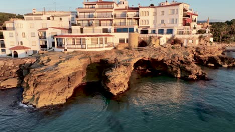 A-spacious-resort-built-on-a-rocky-cliff-is-bathing-in-sunlight,-while-warm-waters-of-Balearic-sea-hit-the-shore