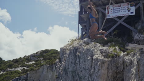 Young-woman-jumps-into-blue-water-off-of-cliffside-on-Greek-island,-slow-motion