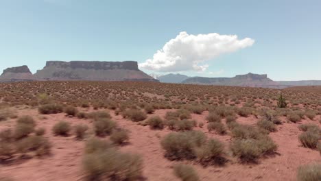 Sweeping-long,-low-aerial-across-scrub-desert,-rock-mesas-in-distance