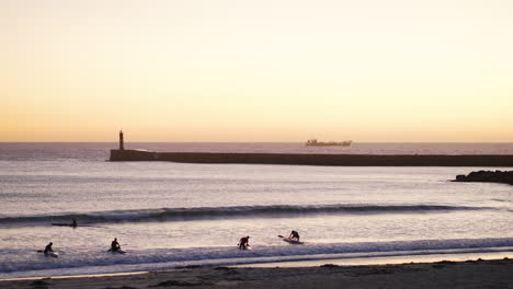 Static-view-of-group-with-kayaks-getting-over-the-surf-at-sunset,-breakwater-and-cargo-ship-backdrop