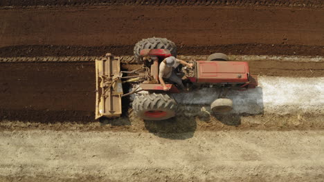 Top-down-shot-of-a-red-tractor-working-in-the-field,-old-tractor-fertilizing-the-soil,-cenital-view