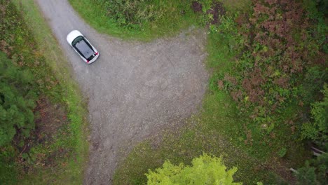 Aerial-view-of-a-e-car-leaving-a-parking-lot,-in-the-forests-of-Switzerland---top-down,-drone-shot