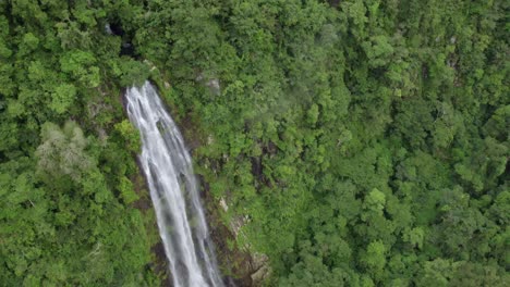 Aerial-dolly-out-of-Las-Lajas-waterfall-falling-into-rocky-pond-surrounded-by-dense-rainforest-and-clouds,-San-Luis-Morete,-Costa-Rica