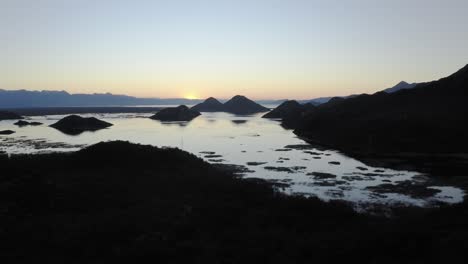AERIAL---Lake-Skadar-and-silhouette-of-mountains-at-sunrise,-Montenegro,-reverse
