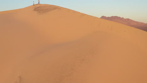 Rising-aerial-of-a-sand-dune-in-the-desert-with-2-people-standing-on-top-of-the-mountain