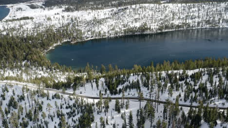 Aerial-of-a-partially-frozen-Cascade-Lake-in-Lake-Tahoe-California-with-cars-moving-along-highway-89
