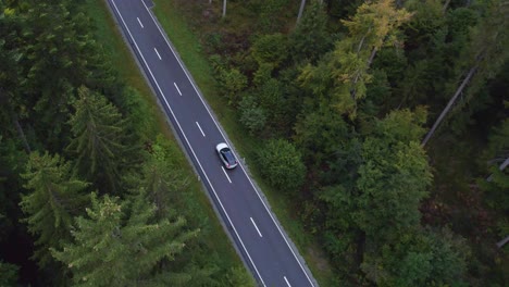 Aerial-view-following-a-electric-SUV-on-a-Swiss-mountain-forest-road---high-angle,-drone-shot