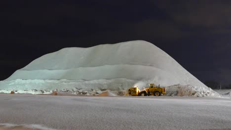 Wide-view-Heavy-machinery-working-on-clearing-streets,-Huge-snow-pile-at-night