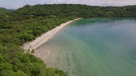 Aerial-dolly-in-of-dense-green-rainforest-coast,-sand-shore-and-turquoise-sea-in-Nacascolo-beach,-Papagayo-Peninsula,-Costa-Rica