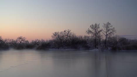 Steam-rising-off-a-frozen-lake-with-trees-silhouetted-by-the-sunrise
