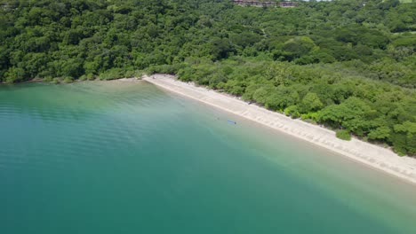 Aerial-truck-left-of-turquoise-sea,-sand-shore-and-dense-green-rainforest-coast-in-Nacascolo-beach,-Papagayo-Peninsula,-Costa-Rica