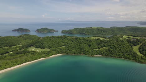Aerial-pan-right-of-green-rainforest-coast-and-turquoise-sea-in-Nacascolo-beach-on-a-cloudy-day,-Papagayo-Peninsula,-Costa-Rica