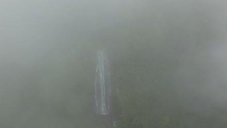 Aerial-dolly-out-of-clouds-over-Las-Lajas-misty-waterfall-streaming-in-rocky-pond-surrounded-by-woods,-San-Luis-Morete,-Costa-Rica