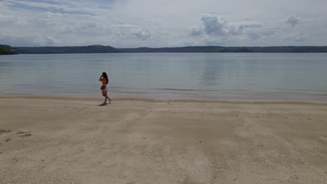 Aerial-rising-of-young-woman-walking-in-sand-shore-near-turquoise-sea-and-forest-in-Nacascolo-beach,-Papagayo-Peninsula,-Costa-Rica