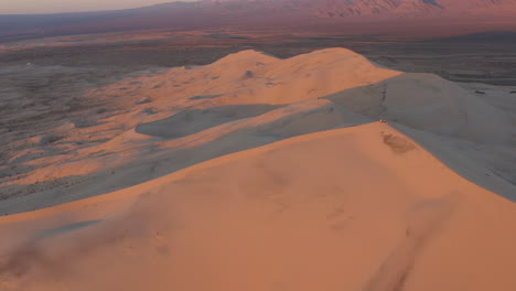 Aerial-of-a-desert-Kelso-Dunes-at-sunset,-long-zoom-out-reveal