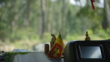 Bhudda-Statue-And-Sri-Lanka-Flag-In-Car-Interior-Moving-On-Road-In-Forest-Area-Full-Of-Green-Trees,-Colombo,-Sri-Lanka