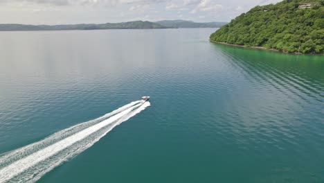 Aerial-dolly-in-of-boat-sailing-in-turquoise-sea-near-hillside-covered-in-forest-in-Nacascolo-beach,-Papagayo-Peninsula,-Costa-Rica
