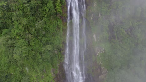 Aerial-rising-over-Las-Lajas-misty-waterfall-surrounded-by-green-dense-rainforest-and-clouds,-San-Luis-Morete,-Costa-Rica