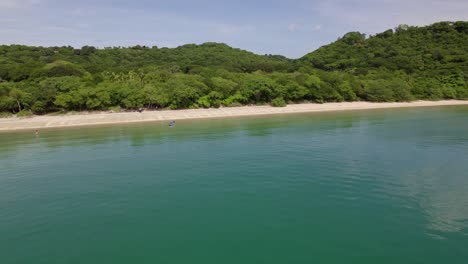 Aerial-truck-right-of-turquoise-sea,-sand-shore-and-dense-green-woods-in-Nacascolo-beach,-Papagayo-Peninsula,-Costa-Rica