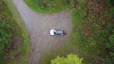 Aerial-view-of-a-person-walking-to-a-suv-trunk-at-a-forest-parking-lot---overhead,-drone-shot