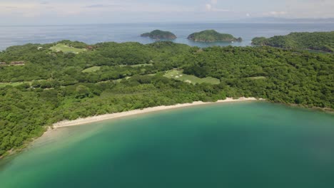 Aerial-dolly-out-of-turquoise-sea-and-dense-green-rainforest-coast-in-Nacascolo-beach-on-overcast-day,-Papagayo-Peninsula,-Costa-Rica